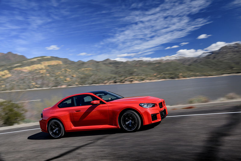 2023 BMW M2 driving on a country road, shown in profile.