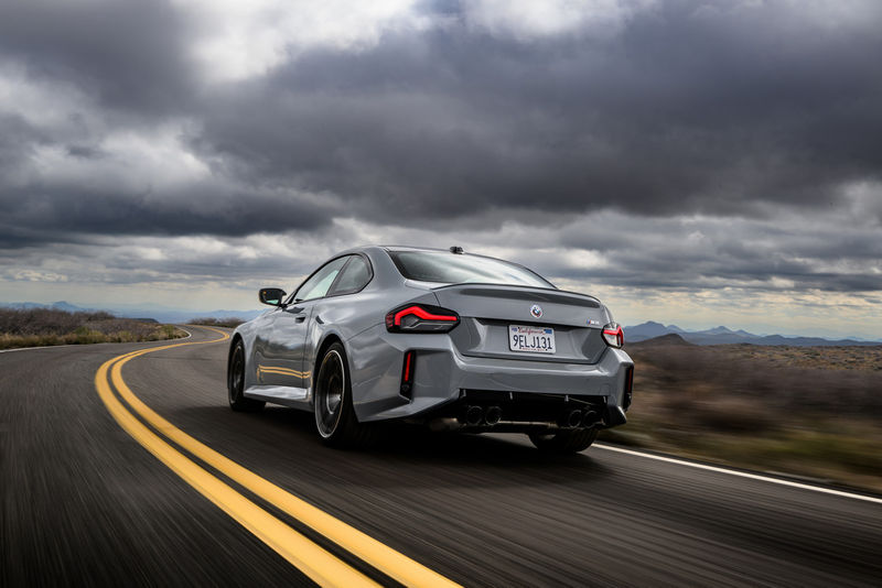 2023 BMW M2 driving on a country road, rear three-quarter view.